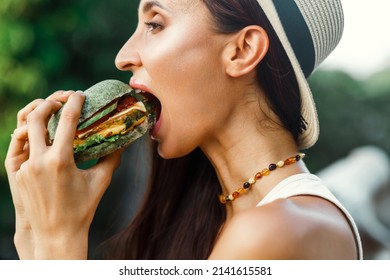 Vegan girl, healthy appearance, holds in her hands and eats a natural, meat-free burger, colored bun, tofu, soy meat, chickpeas. Tropical island Thailand, Bali - Shutterstock ID 2141615581