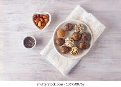 Vegan Healthy Energy Balls With Oatmeal, Chia Seed, Coconut Flakes, Cereals, Cocoa, Dried Fruits And Almond. No Cook Energy Bites On White Plate With Ingredients. Top View.