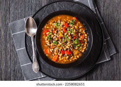 Vegan Hoppin John, savory and spicy black-eyed pea stew in black bowl on dark wood table, southern America recipe, horizontal view from above, flat lay, close-up