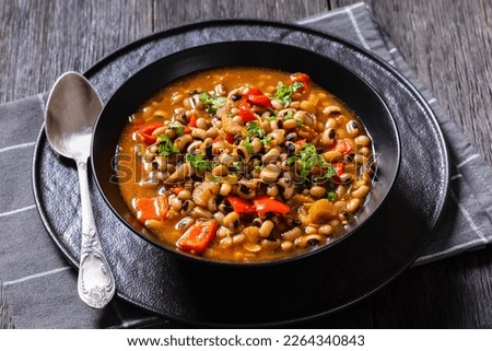 Vegan Hoppin John, savory and spicy black-eyed pea stew in black bowl on dark wood table, southern America recipe, horizontal view