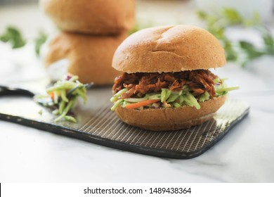 Vegan jackfruit pulled pork sandwich on platter with broccoli slaw on whole wheat buns - Powered by Shutterstock