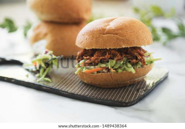 Vegan jackfruit pulled pork sandwich on\
platter with broccoli slaw on whole wheat\
buns