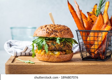 Vegan lentil burger with arugula, mustard sauce, fresh vegetables and sweet potato fries on a wooden board. Vegan food concept.