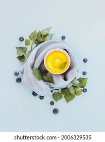 Vegan, Natural Ice Cream Or Frozen Yogurt.Yellow, Homemade, Fruit Ice Cream With Blueberries And Green Leaves On A Blue Background. Concept Of Healthy, Natural, Summer Sweets And Snacks. Flat Lay