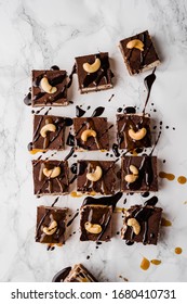 Vegan No-bake Chocolate Date And Coconut Healthy Bites With Peanutbutter And Syrup And Cashew Nut On Top Directly From Above On White Marble