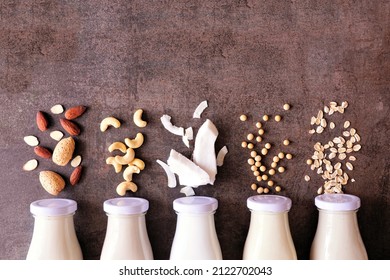 Vegan plant based non dairy milk. Variety in milk bottles with ingredients. Top down view over a brown stone background. - Shutterstock ID 2122702043
