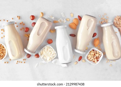 Vegan, plant based, non dairy milk. Variety in milk bottles with scattered ingredients. Above view over a white marble background.