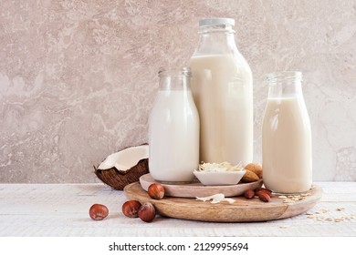 Vegan, plant based, non dairy milk table scene. Coconut, oat and nut in milk bottles with scattered ingredients. Side view against a bright background. - Shutterstock ID 2129995694