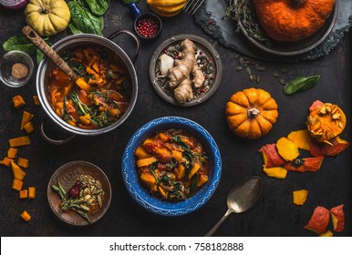Vegan pumpkin stew dish with spinach served in bowl with spoon on dark kitchen table background with pot and ingredients.  Healthy seasonal food and clean eating concept