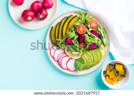 Vegan salad fruits and vegetables dish with avocado, dragon fruit, radish, pumpkin, tomato, corn salad, lettuce, mizuna and lemon on color background. Healthy food