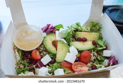 Vegan Salad Made From Avocado, Quinoa, Mixed Leaves, Tomatoes, Vegan Feta And Pomegranate Dead’s In Carton Box With Clear Window On The Middle Served With Wooden Fork And Sauce In A Pot. Healthy Food