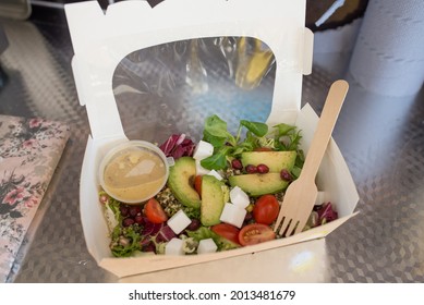 Vegan Salad Made From Avocado, Quinoa, Mixed Leaves, Tomatoes, Vegan Feta And Pomegranate Dead’s In Carton Box With Clear Window On The Middle Served With Wooden Fork And Sauce In A Pot. Healthy Food