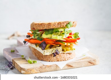 Vegan sandwich with tofu, pepper, carrots, hummus and green dressing on the board. - Powered by Shutterstock