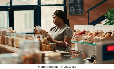 Vegan shopper looking at homemade sauces or dressings to buy additives free bulk products from local zero waste eco store. Woman examining jars with pasta or spices, ecological goods. - Powered by Shutterstock