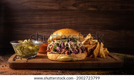 vegan Smoked pulled Jackfruit burger with pickles and sauce and potato wedges on a wooden board and wooden background
