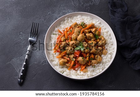 Vegan stew soy meat and vegetables served with boiled rice and greens on black textured background. delicious healthy diet food