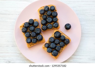 Vegan Toasts With Peanut Butter, Blueberries And Chia Seeds On A Pink Plate Over White Wooden Background, Overhead View. Flat Lay, From Above.