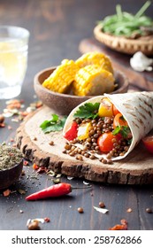 Vegan tortilla wrap, roll with grilled vegetables and lentil  and boiled corn cob on a wooden background