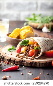 Vegan tortilla wrap, roll with grilled vegetabes and lentil  and boiled corn cob on a wooden background