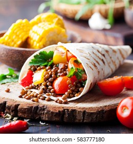 Vegan tortilla wrap, roll with grilled vegetables and lentil and boiled corn cob on a wooden background.
