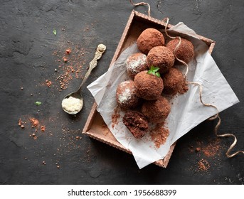 Vegan Truffle. Chocolate Potato Cake On White Paper In A Box And A Spoon With Coconut Powder On A Black Background. Top View. Flat Lay