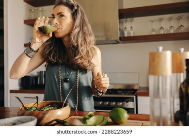 Vegan woman drinking some green juice while having a buddha bowl. Mature woman serving herself a healthy plant-based meal in her kitchen. Senior woman eating clean at home. - Powered by Shutterstock