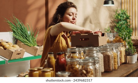 Vegan woman in specialty zero waste supermarket counting apples, adding them to shopping basket. Client in local neighborhood grocery shop picking freshly harvested fruits - Powered by Shutterstock