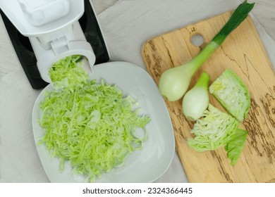 Сabbage in a vegetable cutter on kitchen table. Chopped cabbage is falling into a bowl. Homemade healthy food.