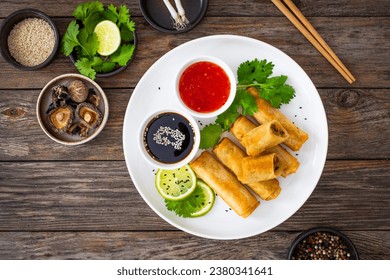 Vegetable filled spring rolls and sauces on wooden table 