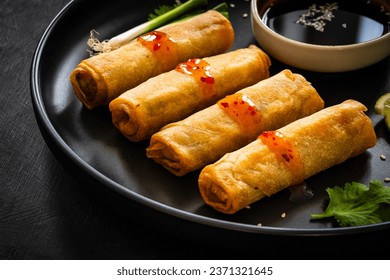 Vegetable filled spring rolls and soy sauce on black wooden table 