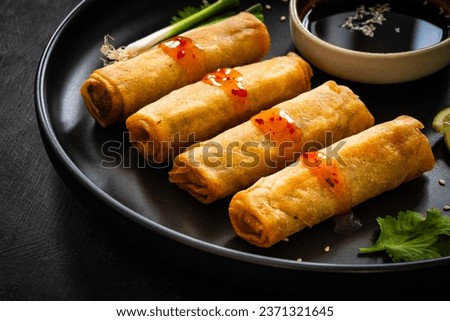 Vegetable filled spring rolls and soy sauce on black wooden table 