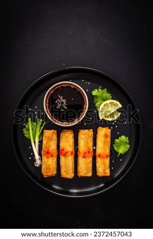 Vegetable filled spring rolls and soy sauce on black wooden table 