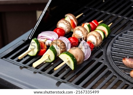 Vegetable kebabs, with courgette, red onion, red pepper, mushroom and tomato, cooking on a gas barbecue.