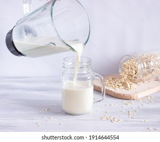 Vegetable Oat Milk Is Poured From A Blender Into A Glass Glass On A Light Background. Preparation Of Vegetable Milk. Healthy Drinks, Vegetarianism. Side View.