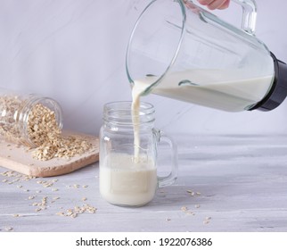 Vegetable Oat Milk Is Poured From A Blender Into A Glass Glass On A Light Background. Preparation Of Vegetable Milk. Healthy Drinks, Vegetarianism. Side View.