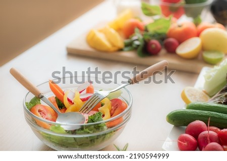 Vegetable salad in clear glass bowl and cutlery On the kitchen table, there are vegetables and fruits such as tomatoes, cucumbers, bell peppers, lettuce, radishes and lemons.
