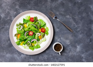 Vegetable salad consists of Red Oak, Green Oak, Tomato, Onion, Lettuce, Kep Kus Berry. Served with sesame dressing Packed in a white ceramic plate with gray edges. With a fork on an old dark gray.  - Shutterstock ID 1402127591
