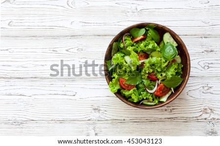 Vegetable salad with fresh lettuce, tomatoes and cucumber in clay pot. Top view.