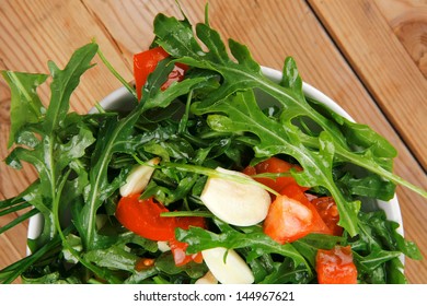 vegetable salad : green salad with raw tomato and garlic in white bowl over wood served with cutlery