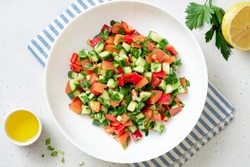 Vegetable Salad In A White Plate On A Light Background Top View. Salad With Tomatoes, Cucumbers, Peppers, Parsley And Lemon. Vegan Or Diet Food.