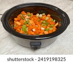 Vegetable soup in oval slow cooker with carrots sweet potato and celery sitting on kitchen bench