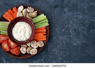 Vegetable Tray With A Ranch Dip On A Dark Background. Raw Vegetable Mix Includes Sliced Mushrooms, Carrots, Celery, Tomatoes.