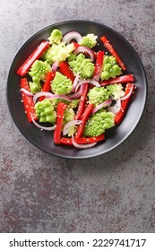 Vegetable vegan salad of Romanesco broccoli, bell pepper and red onion sprinkled with sesame seeds close-up in a plate on the table. Vertical top view from above
