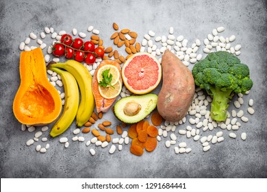 Vegetables, fruit and foods containing potassium over gray stone background, top view. Natural sources of potassium, vitamins and micronutrients for healthy balanced diet and avitaminosis prevention