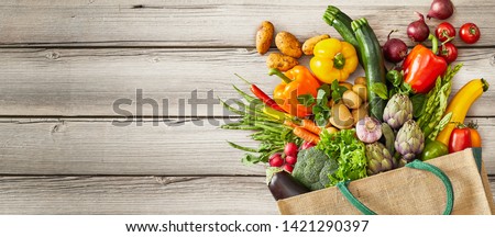 Vegetables and fruits falling out of tipped over bag next to large empty space over rustic wooden background