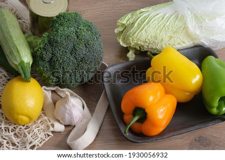 vegetables in a mesh shopping bag and plastic wrapped on a rustic kitchen table, say no to plastic, using reusable shoppers, zero waste lifestyle, plastic bags and food trays versus eco bag