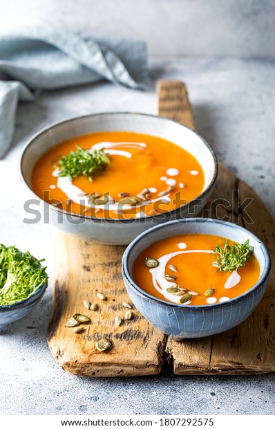 Vegetarian autumn pumpkin and carrot soup with\
cream, seeds and cilantro micro greens. Comfort food, fall and\
winter healthy slow food\
concept