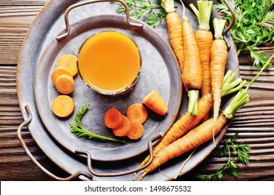 Vegetarian background of old fashioned tray with fresh organic carrots and juice on kitchen wooden table. Top view.