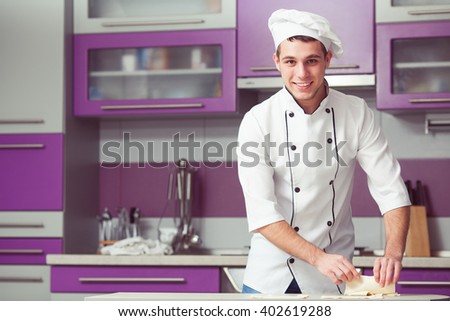 Vegetarian bakery concept. Smiling chef cook in uniform making slices of puff pastry, cooking french chausson. Indoor shot