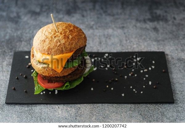 Vegetarian burger made of eggfruit hamburger, with\
cheese, onion, tomato and cheese and integral bun. On textured\
black board. 